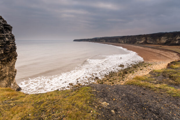 Small bay with lapping waves under grey skies.