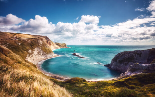 Image of Durdle Door in Dorset. Turquoise waters in a bay under blue sky and white cloud.